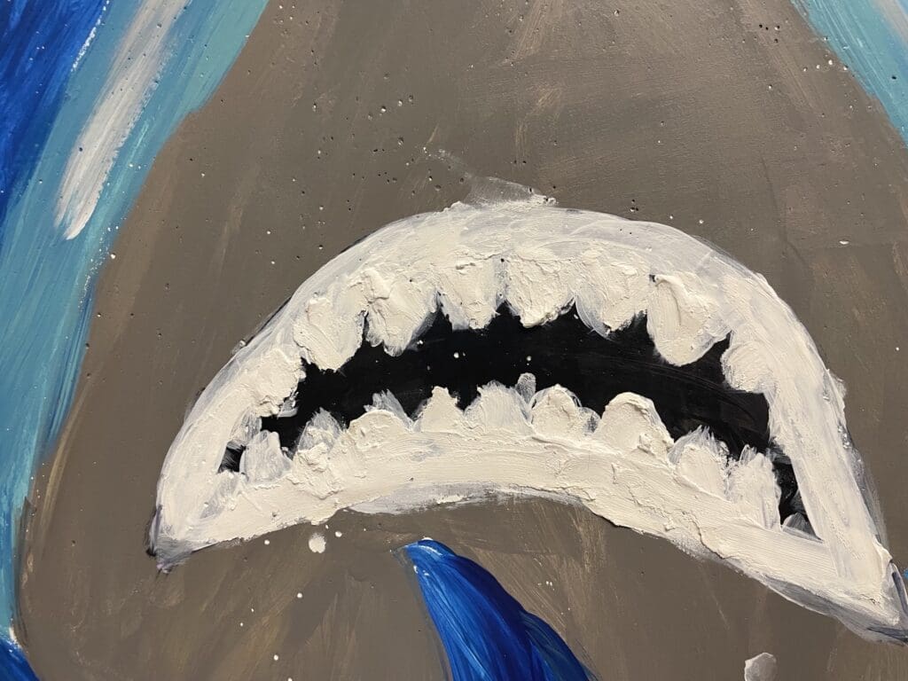 A handmade shark jaw craft with sharp teeth and a blue fin.