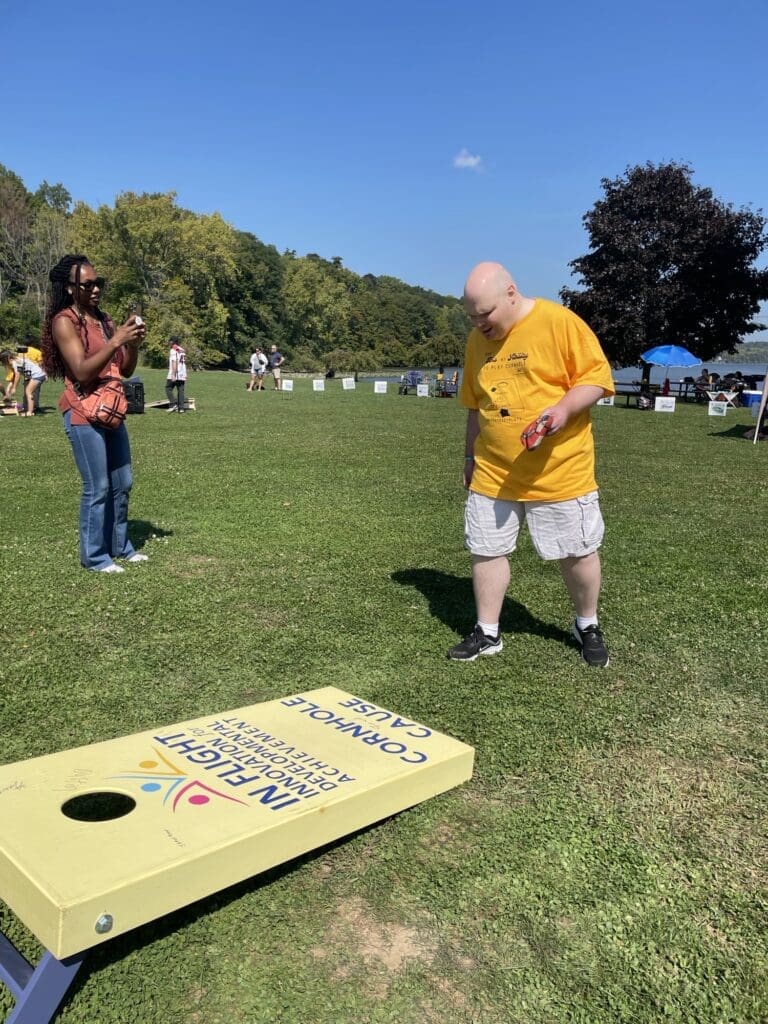 Two men playing cornhole on a sunny day in the park.