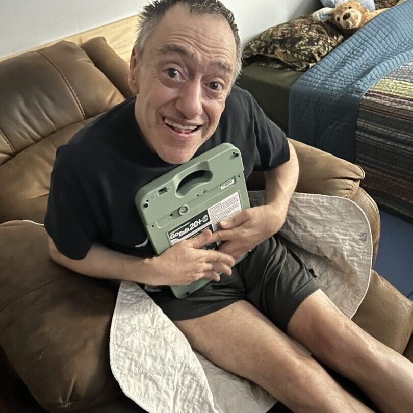A joyful man holding a green game console while sitting on a couch.