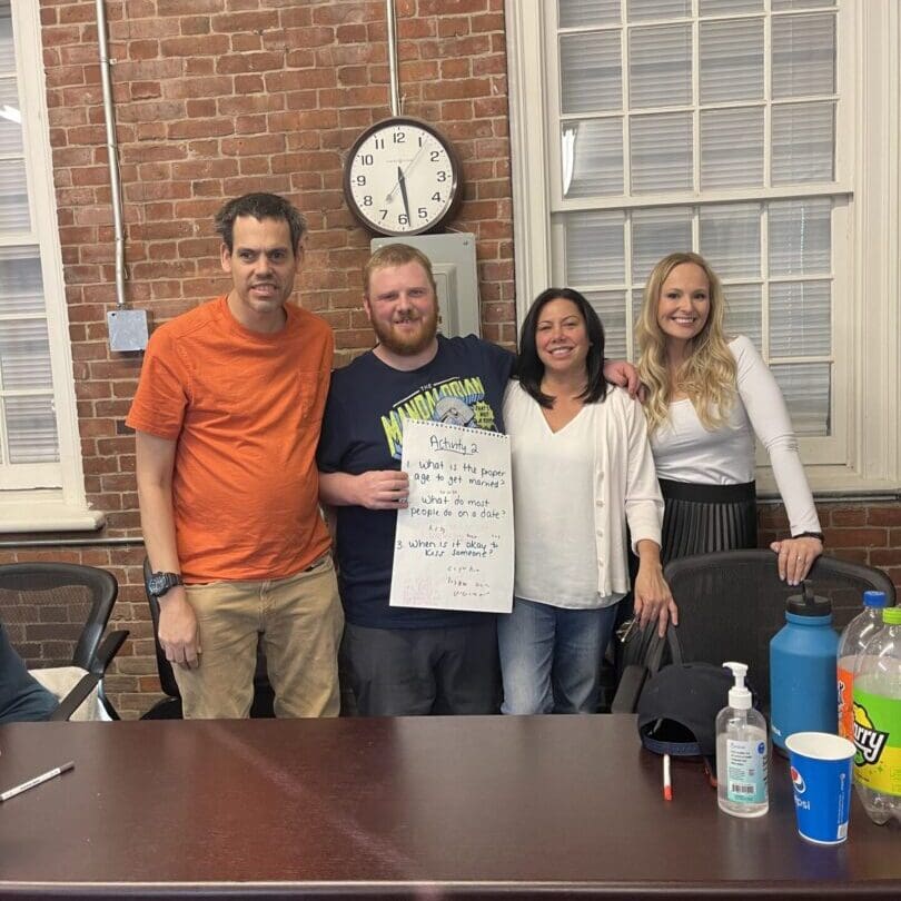 Four people standing indoors holding a poster with cleaning supplies on the table.