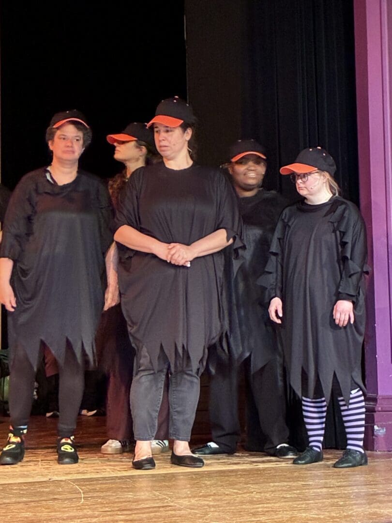 Five performers on stage in black costumes