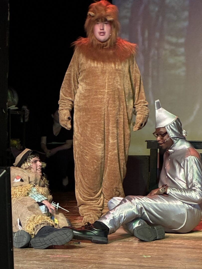 Three actors in lion, scarecrow, tin man costumes